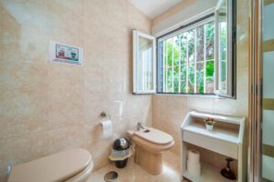 Modern bathroom interior featuring a bidet, toilet, and open window with outdoor view.